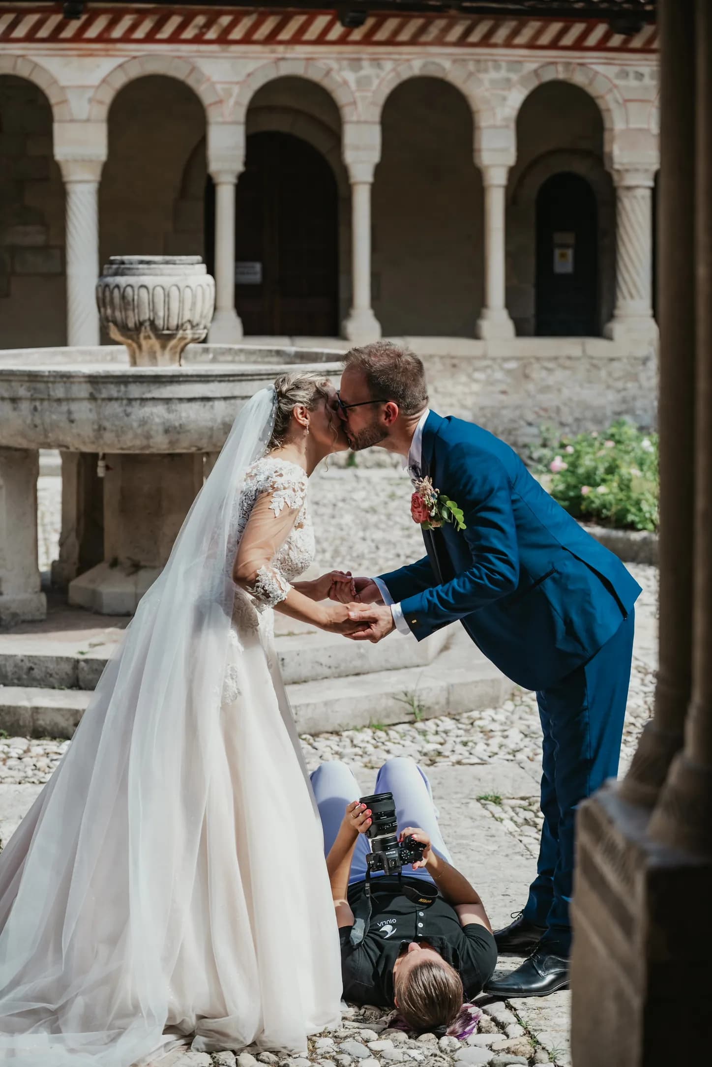 Giulia sdraiata in un chiostro fotografa due sposi che si baciano