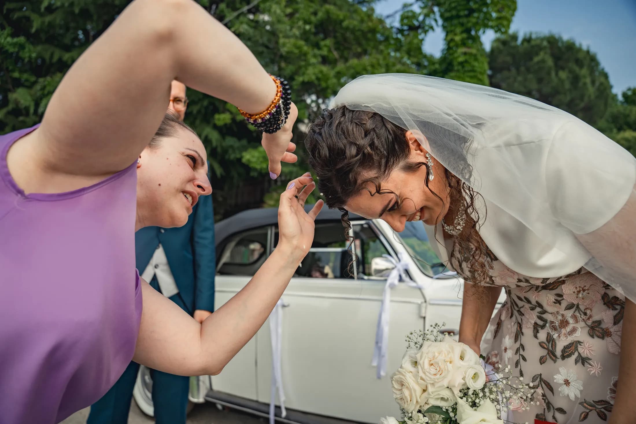 Giulia sistema i capelli della sposa accanto a un’auto d’epoca