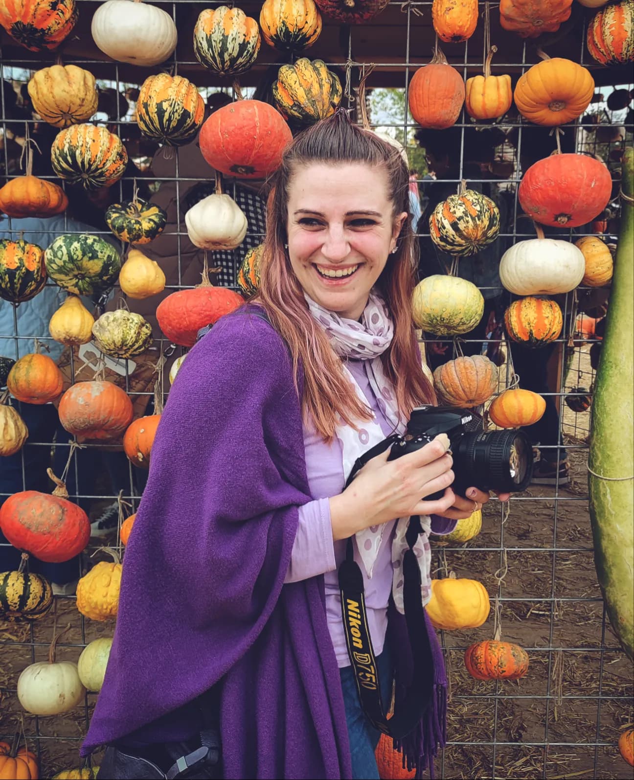 Giulia sorride con la macchina fotografica davanti a una parete di zucche