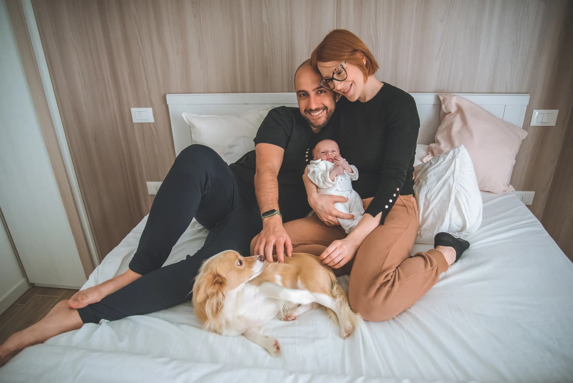 Una famiglia sul letto di casa con il neonato e il cane