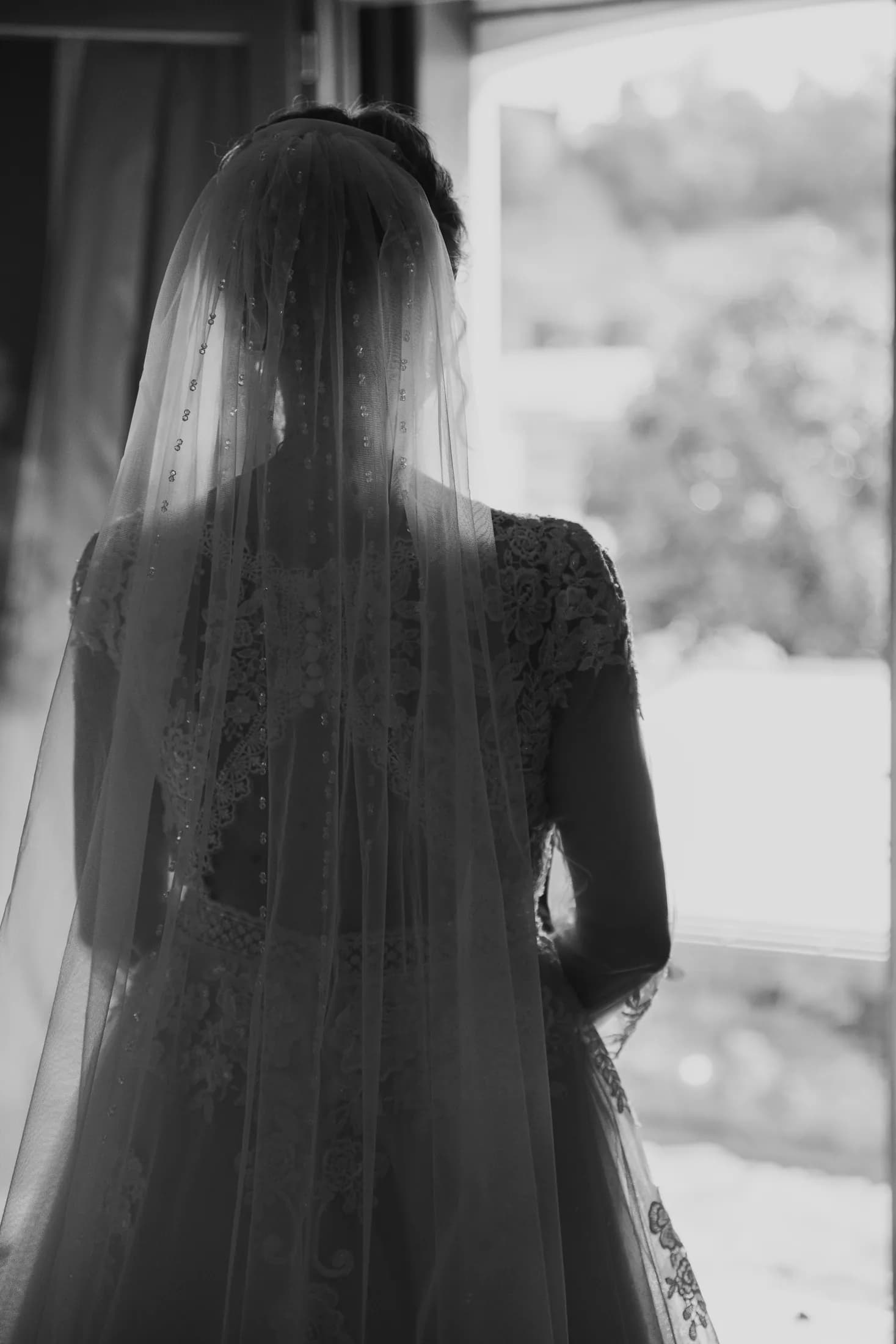 La sposa di spalle con il velo, in bianco e nero, guarda fuori dalla finestra